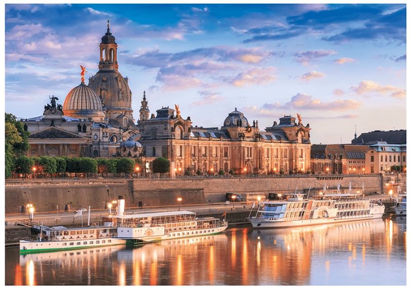 Zwei Passagierschiffe liegen am Flussufer, im Hintergrund historische Gebaeude bei Sonnenuntergang.